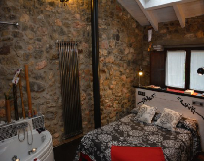 habitacion con paredes de piedra y techo blaco con bañera de hidromasaje triangular al lado de la cama en un hotel en Villafeliz