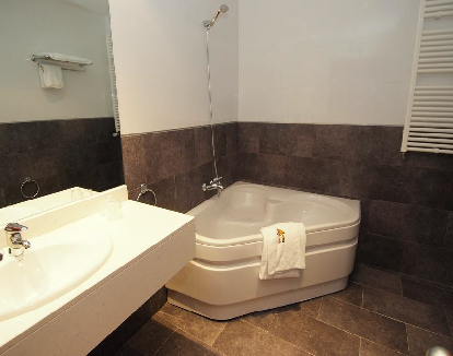 baño de habitacion con paredes blancos y piso de ceramica negra con bañera de hidromaseje triangular en la esquina en un hotel en Haro, La rioja
