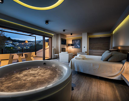 Foto del interior de una habitación con jacuzzi privado, cama para 2 personas y vista de la ciudad