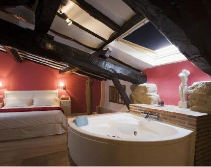 habitacion de paredes rojas con una bañera de hidrosaje triangular al lado de la cama en un hotel en Briñas, La rioja
