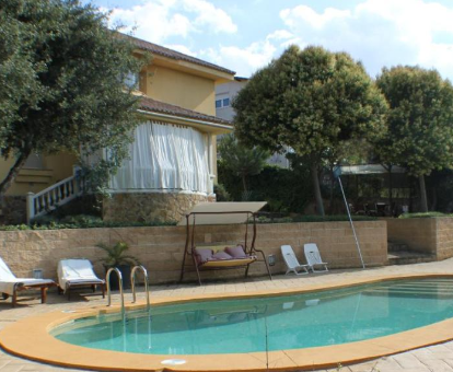 Foto de Villa Lasada donde se muestra su amplia piscina al aire libre, lugares de descanso para tomar el sol y fachada de la Villa