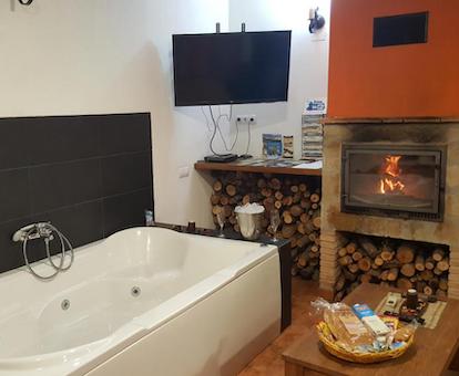 Foto de la bañera de hidromasaje frente al televisor y junto a la chimenea de leña encendida.