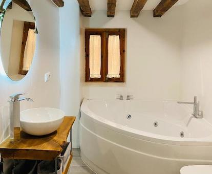 Foto del jacuzzi en el cuarto de baño frente al lavabo y bajo la pequeña ventana de marco de madera y bajo las vigas de madera del techo.