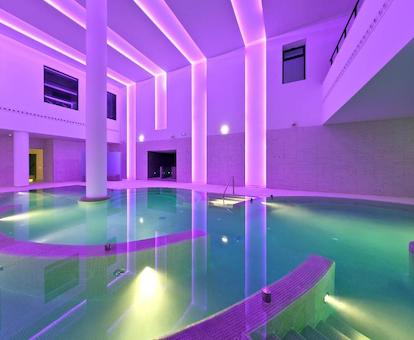 Piscina climatizada de interior con luz rosa en toda la sala y con zonas de chorros de agua para relajarse.