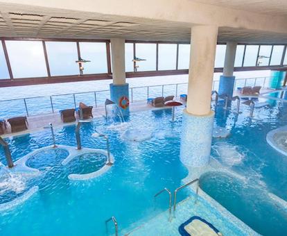 Foto de la piscina climatizada del spa con zonas de chorros de agua, tumbonas sumergidas en el agua y zonas de jacuzzi.